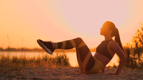 Young-beautiful-woman-athlete-practicing-on-the-beach-doing-exercises-for-the-muscles-of-the-abs-at-sunset.-Twisting-in-slow-motion